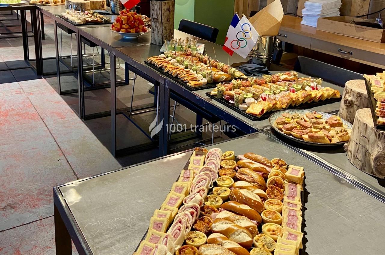 Buffet composé de divers amuse-bouches, tartes salées et pains, décoré avec des drapeaux français et olympiques.