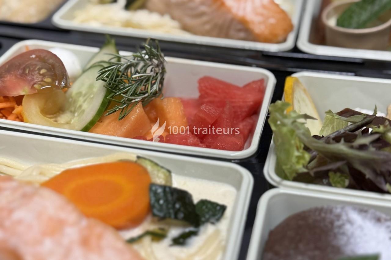 Plateaux-repas contenant des légumes frais, des fruits découpés et des portions de poisson, présentés dans des compartiments.