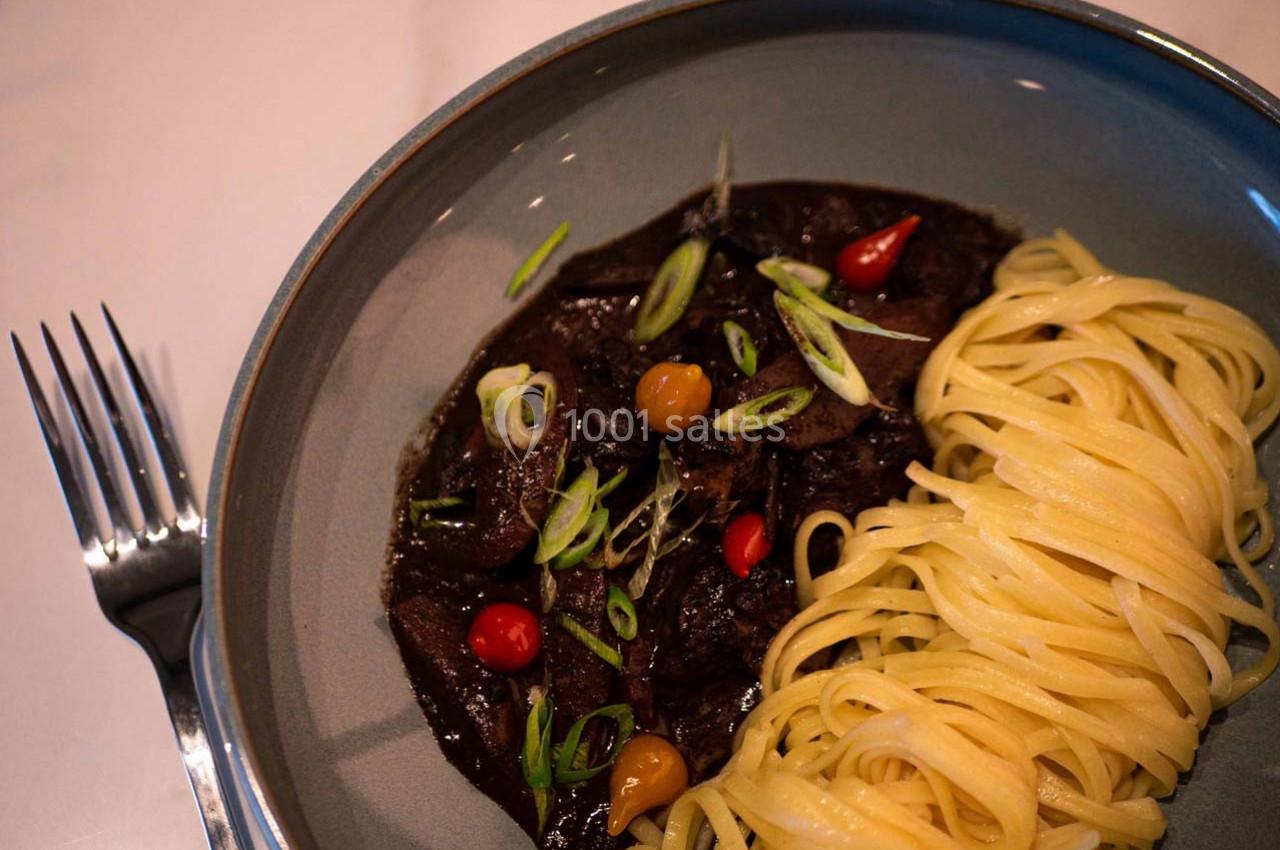 Assiette contenant des pâtes linguine et un ragoût sombre garni de légumes et d'oignons verts émincés.