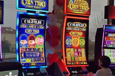 Deux machines à sous lumineuses avec écrans colorés, une personne assise devant l'une d'elles dans un casino.