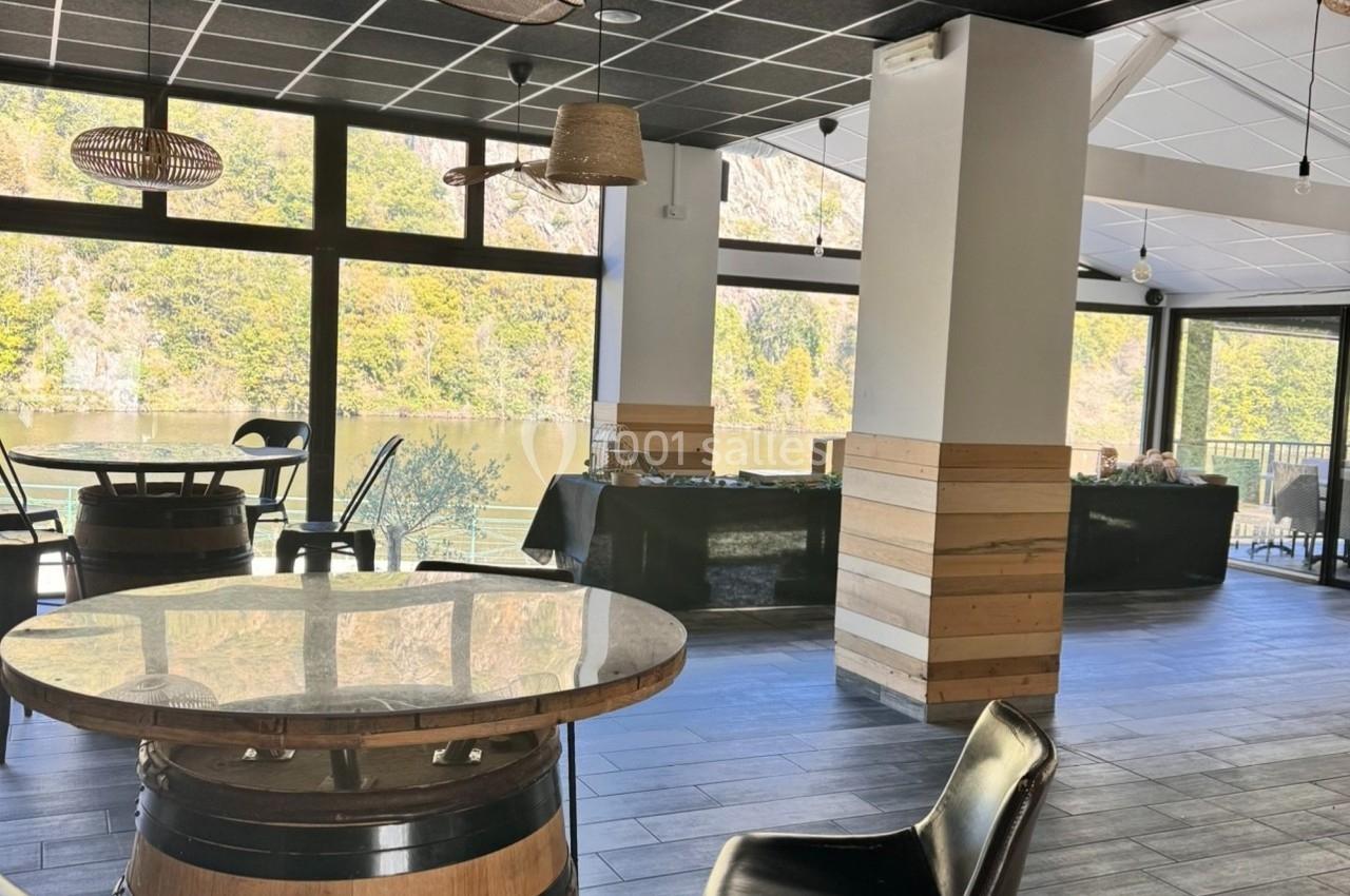 Salle lumineuse avec grandes baies vitrées donnant sur un paysage de lac et de collines verdoyantes.