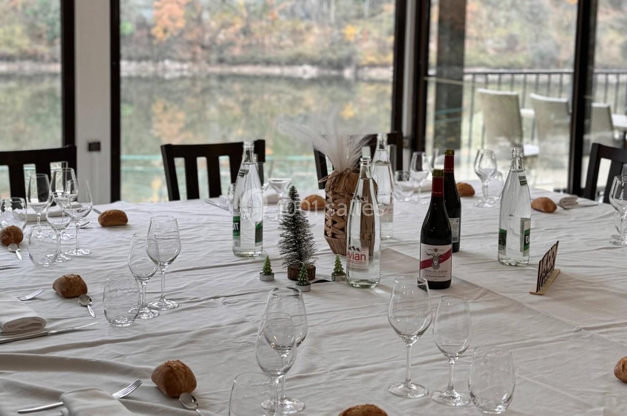 Table dressée avec nappes blanches, verres, bouteilles d'eau et de vin, petits pains et décorations miniatures.