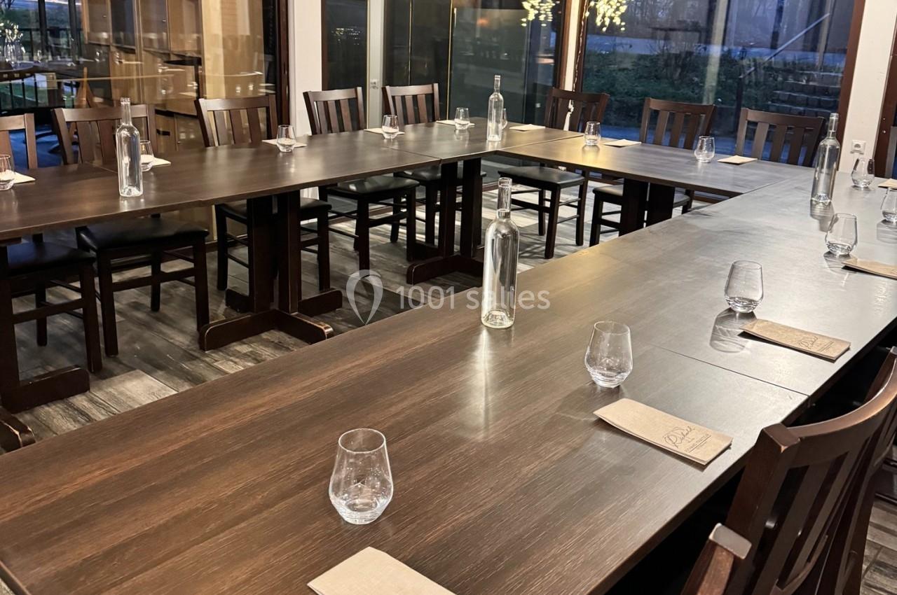 Salle de réunion avec une grande table en bois disposée en U, équipée de verres, bouteilles d'eau et carnets.