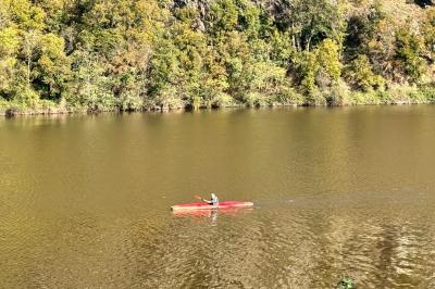 Un kayakiste pagaye sur une rivière calme entourée de végétation et de falaises verdoyantes.
