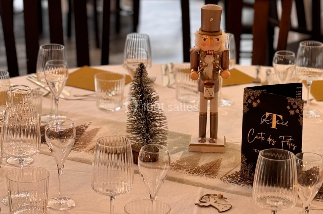 Table décorée pour les fêtes avec un casse-noisette, un petit sapin, des verres et un menu sur une nappe blanche.