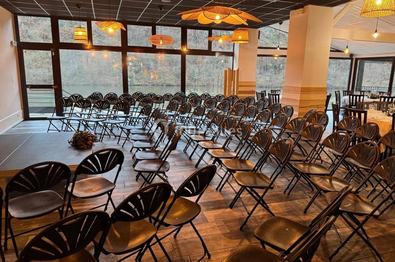 Salle aménagée avec des rangées de chaises noires face à une scène, éclairée par des suspensions lumineuses.