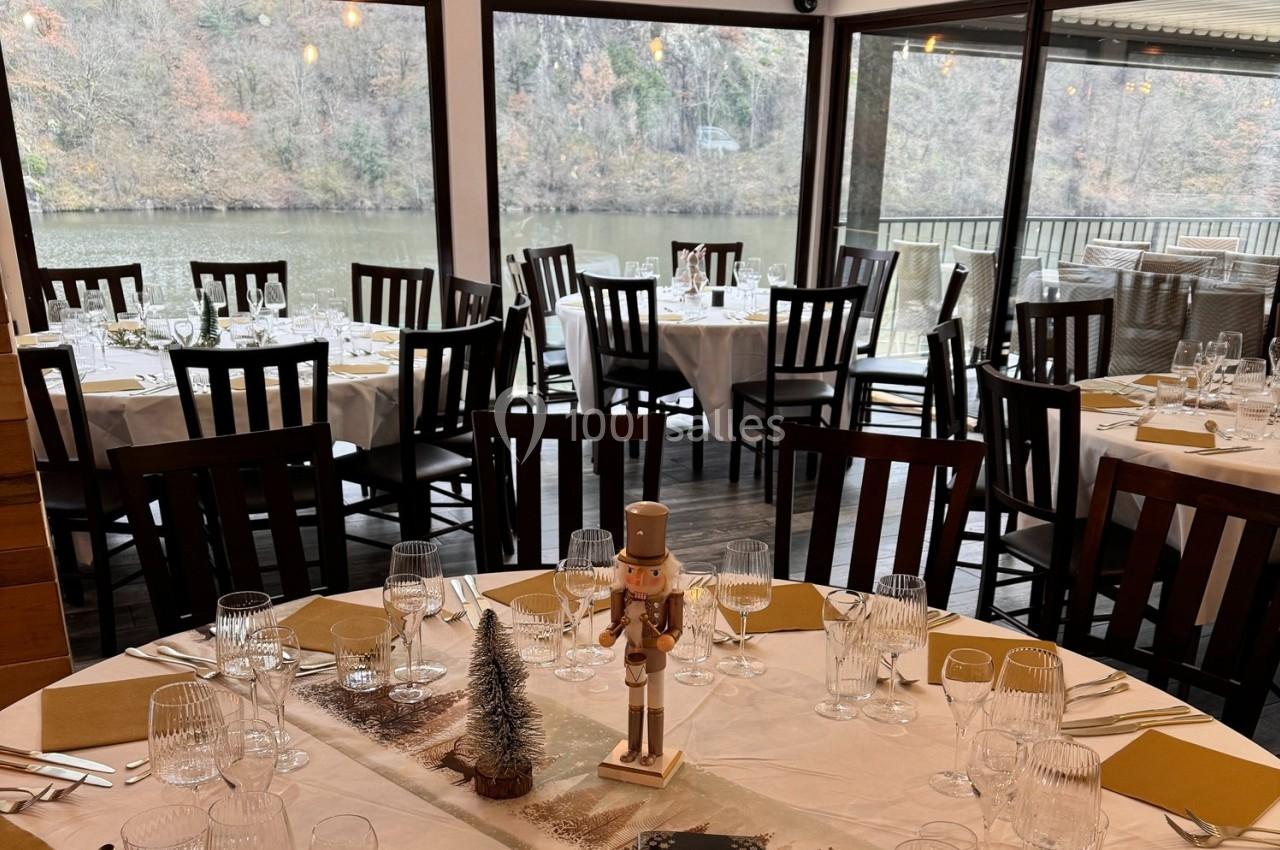 Salle de restaurant avec tables dressées, vue sur une rivière et décorations de Noël au centre des tables.