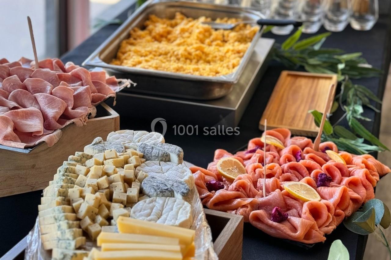 Plateau de charcuterie, fromages variés et saumon fumé avec citron, accompagnés d'un plat chaud en arrière-plan.