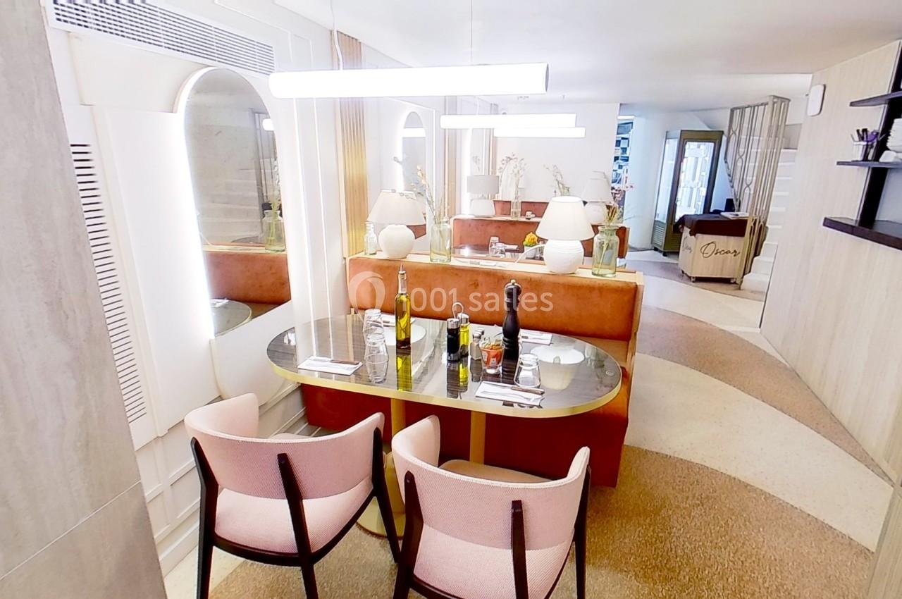 Salle à manger lumineuse avec table ovale dressée, chaises roses, banquette orange et décor moderne.