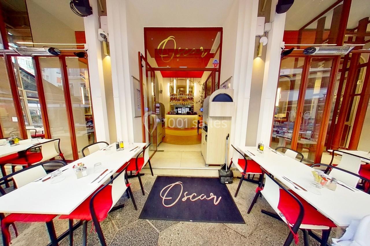 Entrée d'un restaurant avec terrasse, tables dressées et enseigne ’Oscar’ visible au-dessus de la porte.