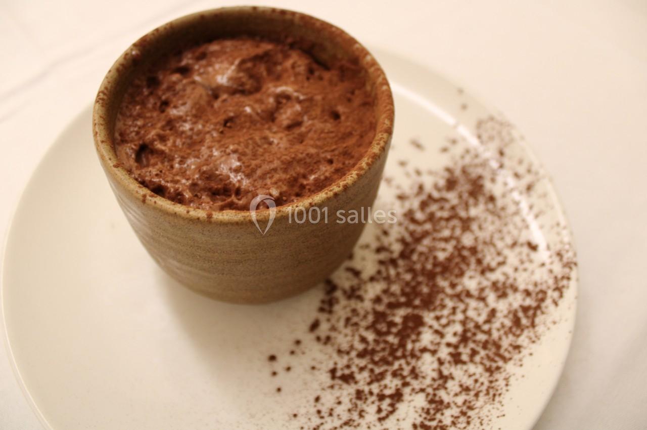 Une mousse au chocolat servie dans un bol en céramique, avec du cacao en poudre saupoudré sur l'assiette blanche.