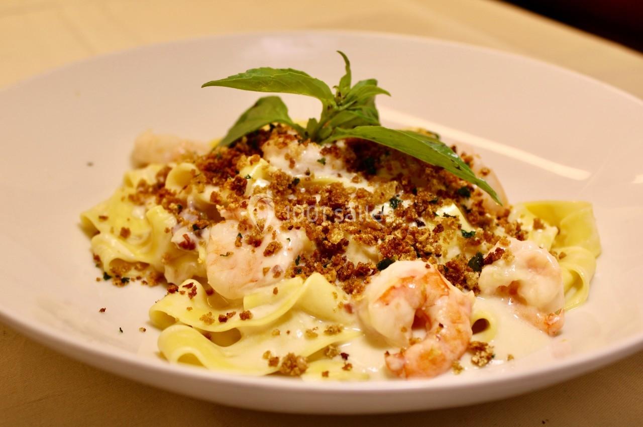 Assiette de tagliatelles garnies de crevettes, chapelure dorée, sauce crémeuse et feuille de basilic en décoration.