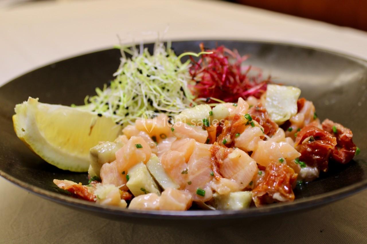 Assiette de tartare de saumon avec citron, germes frais et légumes colorés, servie dans un bol noir.
