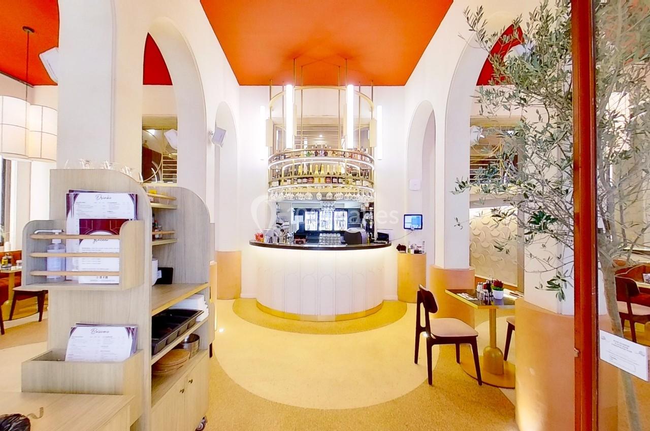 Intérieur d'un restaurant lumineux avec un comptoir central arrondi, des arches blanches et un plafond rouge.