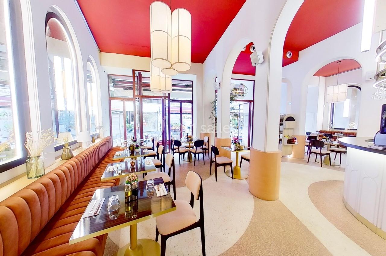 Salle de restaurant lumineuse avec banquettes orange, tables dressées, arches blanches et plafond rouge.