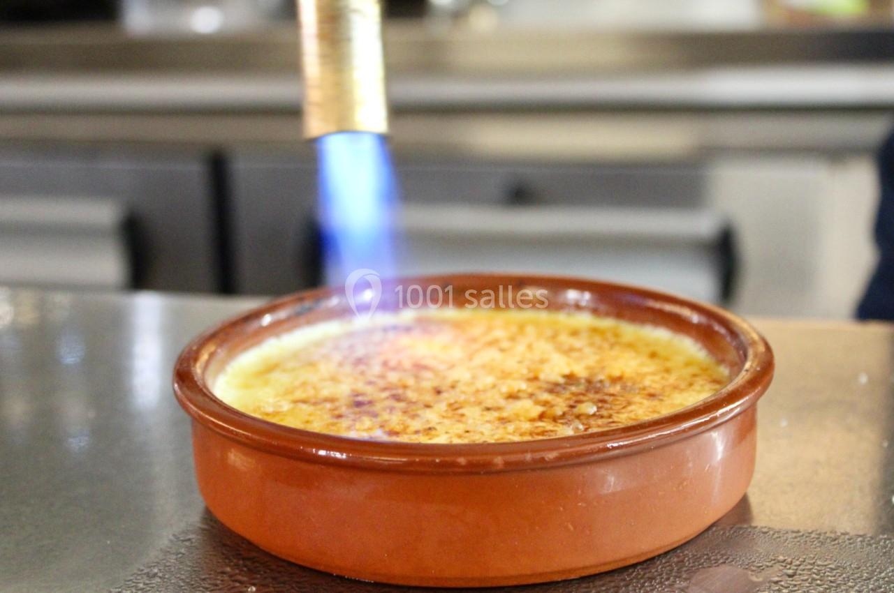 Flamme d'un chalumeau caramélisant la surface d'une crème brûlée dans un plat en terre cuite.