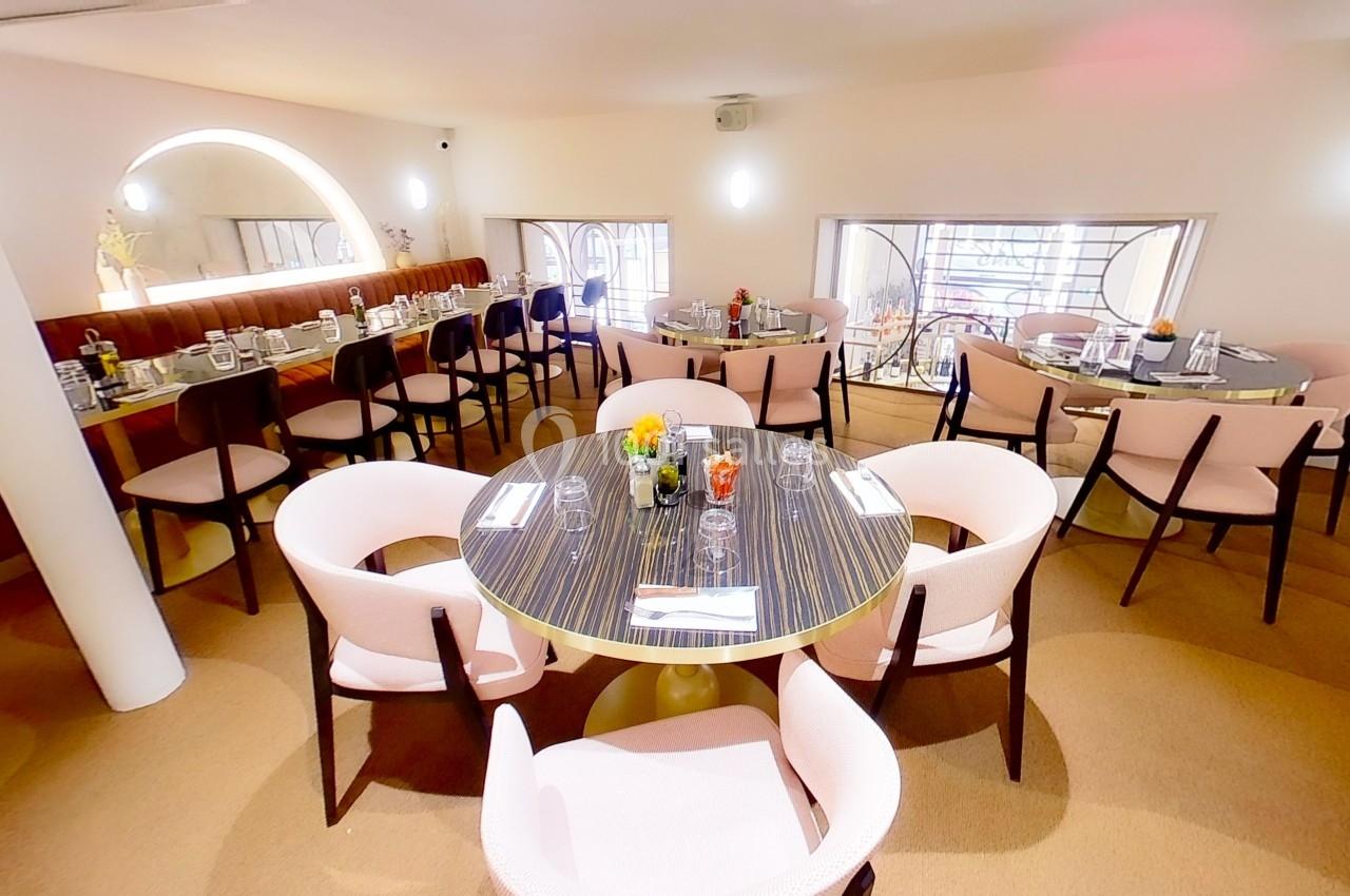 Salle de restaurant lumineuse avec des tables rondes dressées, entourées de chaises roses et une décoration épurée.