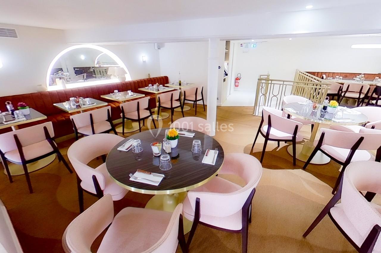 Salle de restaurant lumineuse avec tables rondes, chaises rembourrées roses et décoration élégante.
