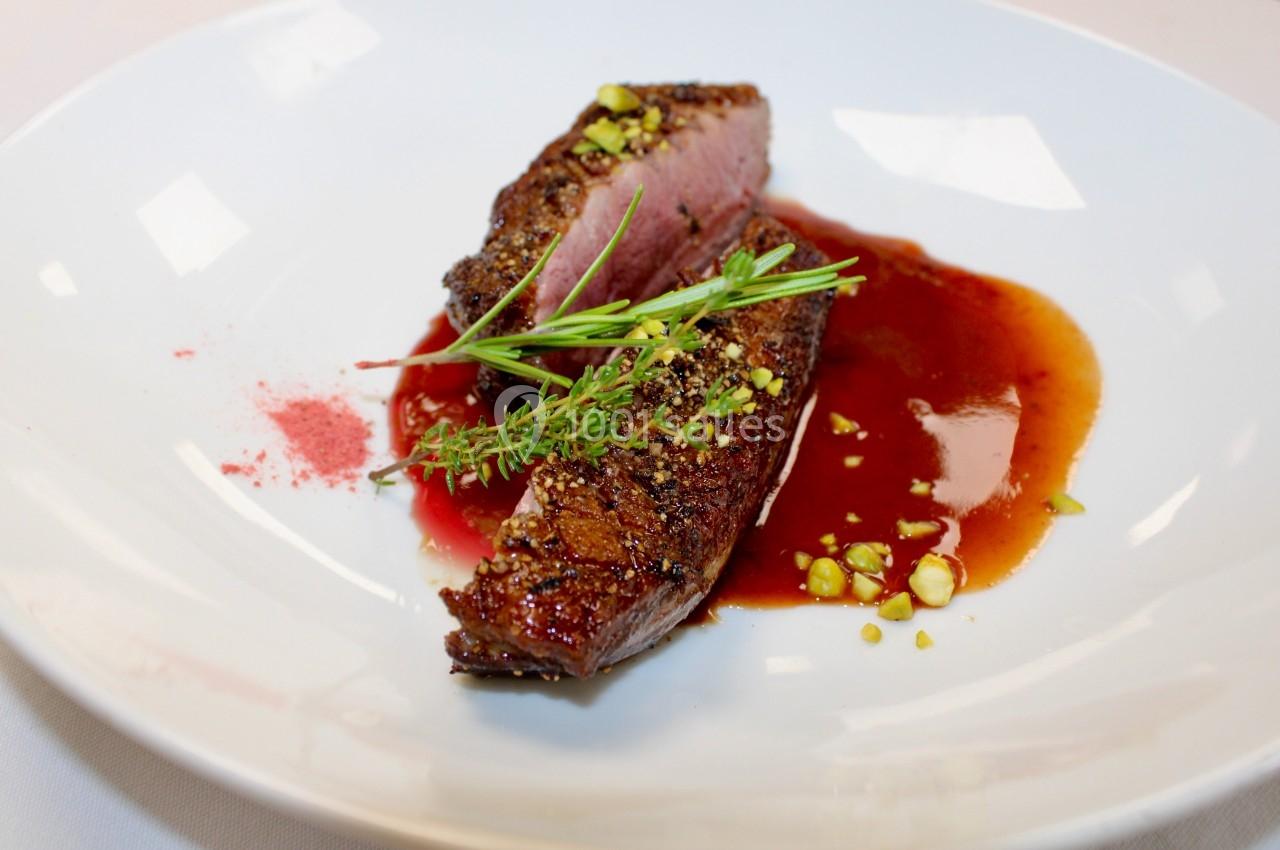 Tranche de viande cuite à point servie avec une sauce rouge, garnie de pistaches concassées et d'herbes fraîches.