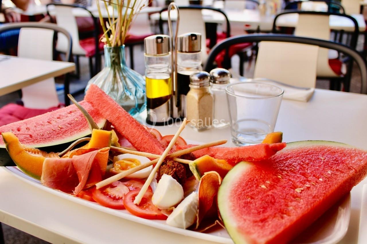 Assiette garnie de fruits frais, légumes, charcuterie et mozzarella, posée sur une table en terrasse.