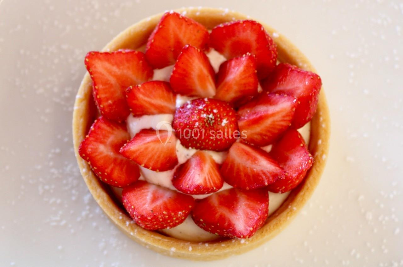 Tartelette garnie de crème et de fraises fraîches disposées en rosace sur une assiette saupoudrée de sucre.