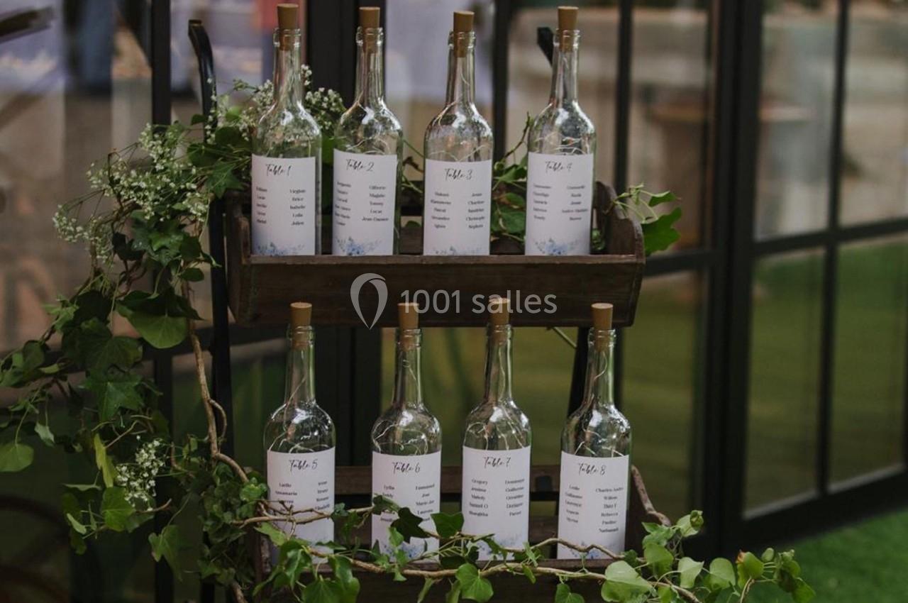Bouteilles en verre alignées sur un présentoir en bois, entourées de feuillage et de petites fleurs blanches.