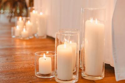 Bougies allumées sur une table décorée avec des verres, assiettes empilées et serviettes pliées.