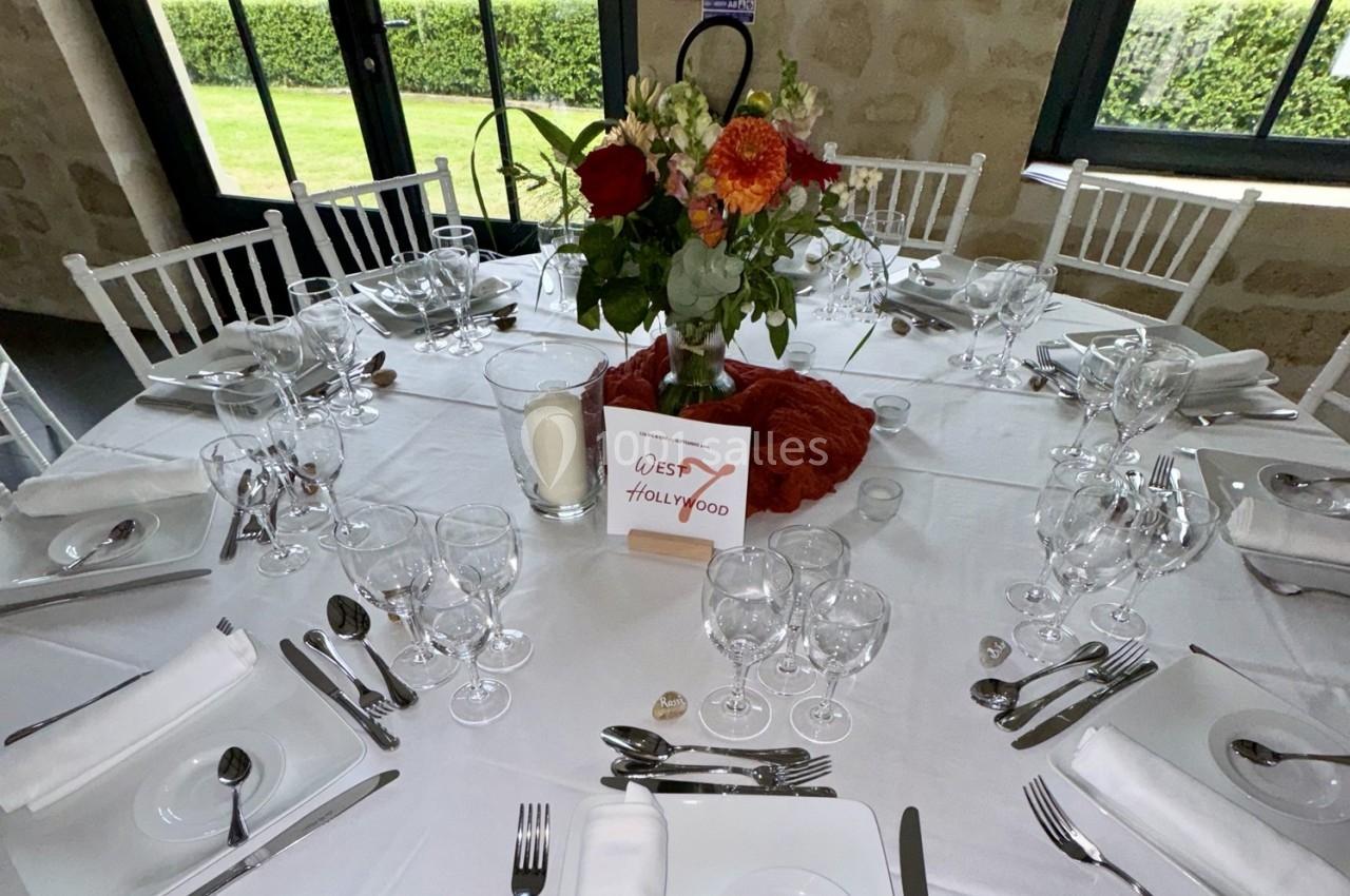Table dressée pour un repas, avec nappes blanches, vaisselle élégante, centre de table floral et pancarte décorative.