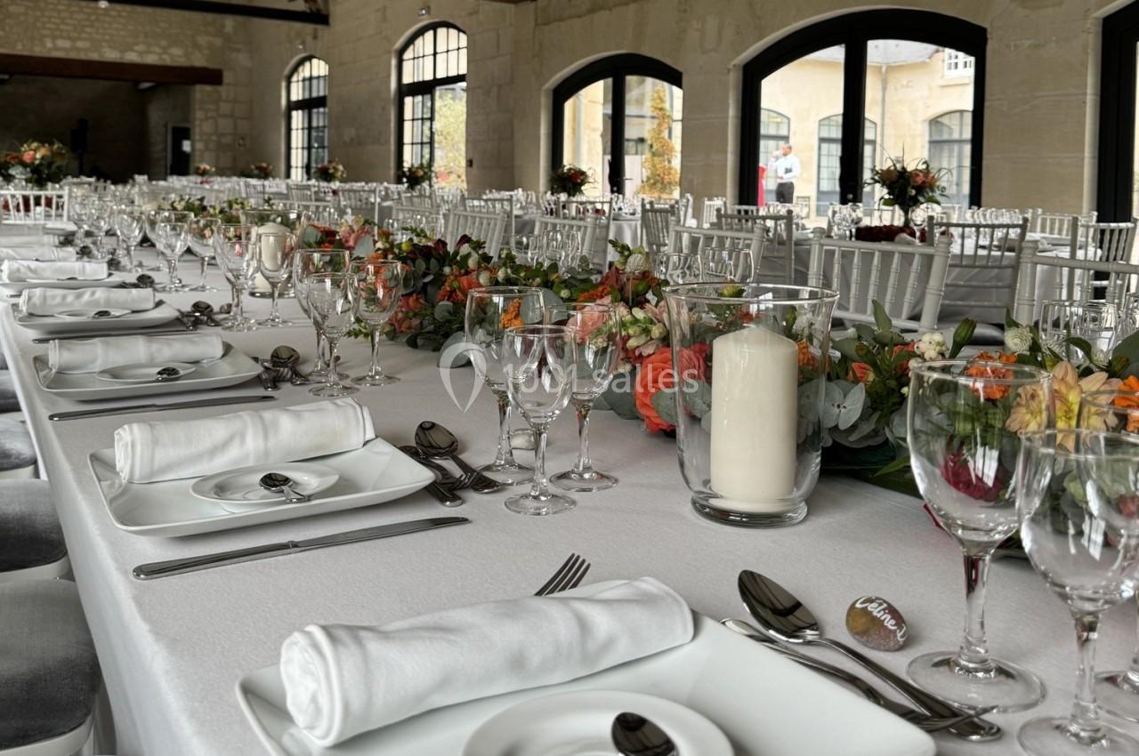 Grande table de réception élégamment dressée avec nappes blanches, vaisselle raffinée et décorations florales colorées.