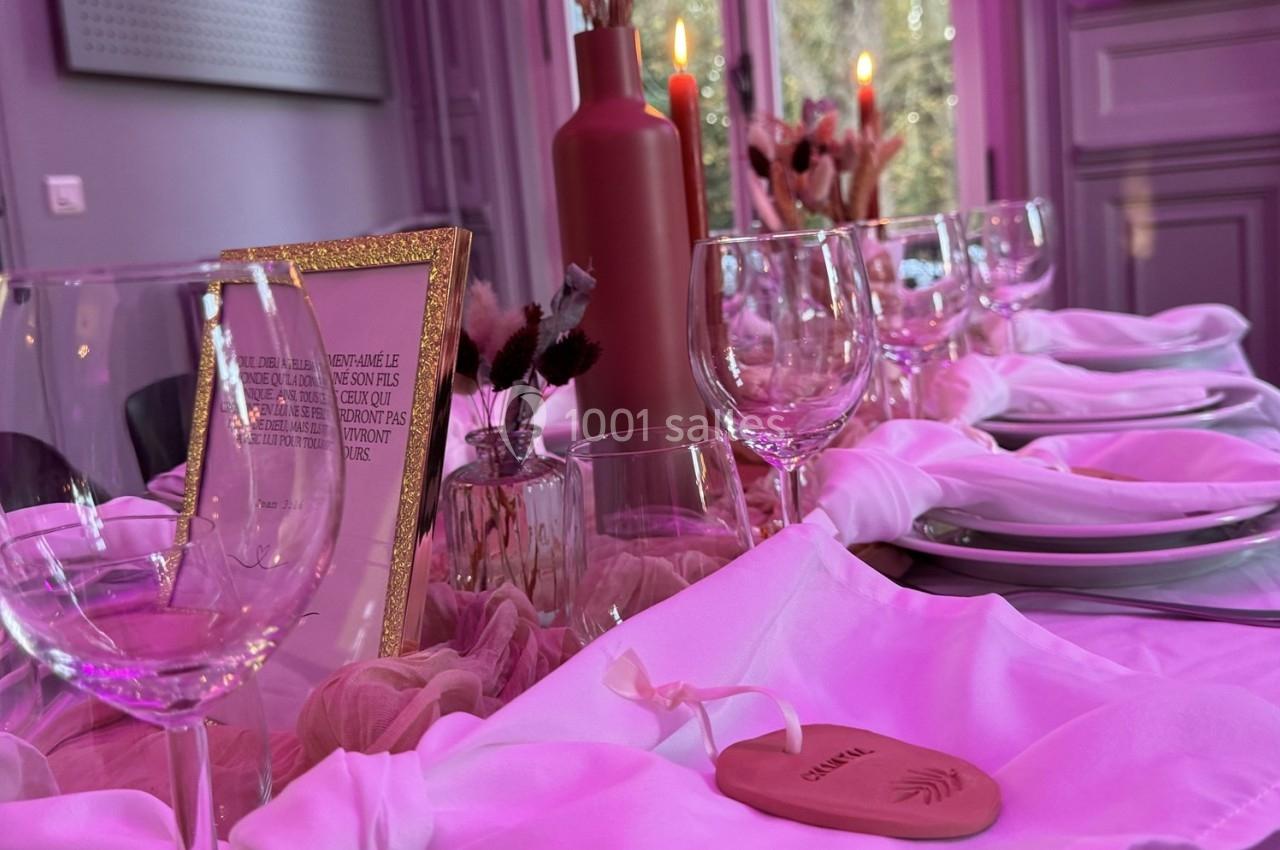 Table élégamment dressée avec nappes blanches, verres, bougies rouges et décorations florales dans une ambiance lumineuse…