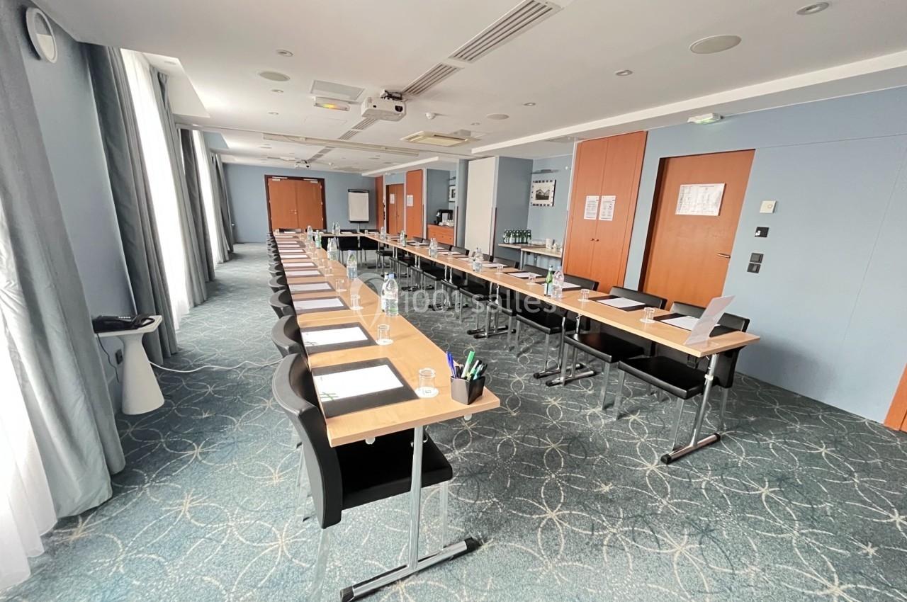 Salle de réunion lumineuse avec tables disposées en U, équipée de matériel de présentation et de fournitures.