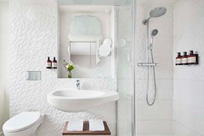 Salle de bain moderne avec lavabo suspendu, douche vitrée, toilettes et murs ornés de motifs en relief.