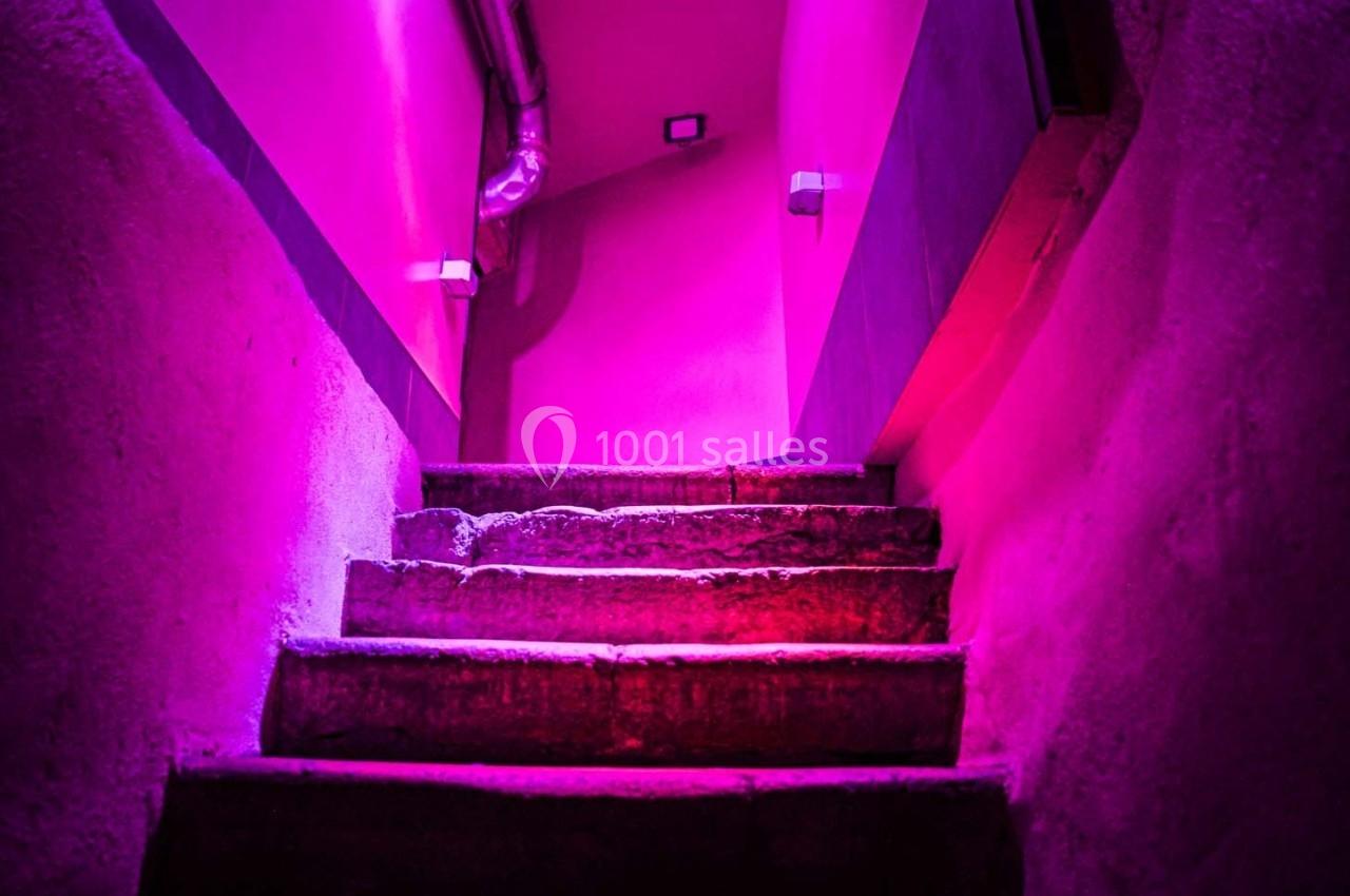Escalier en béton éclairé par une lumière rose intense, menant à un espace fermé avec des murs texturés.