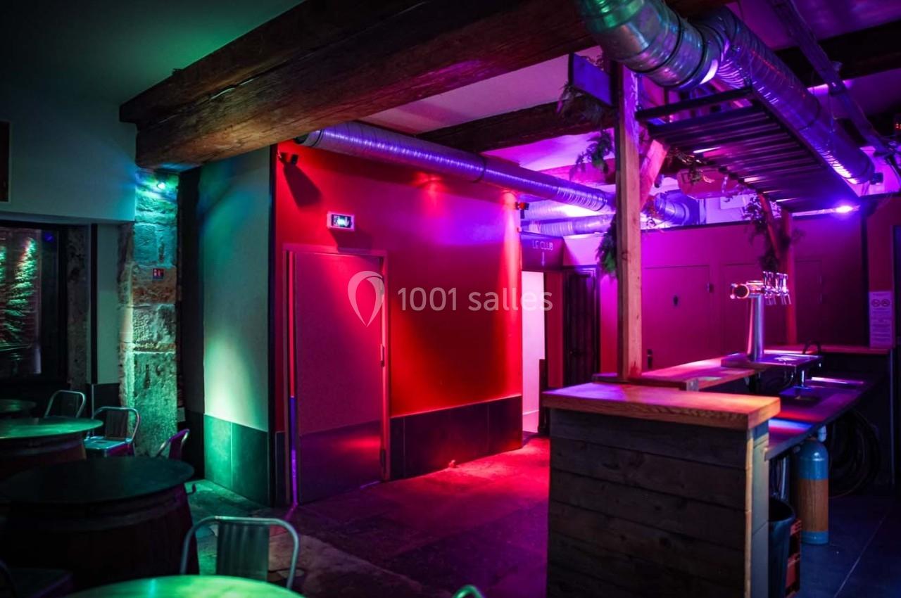 Intérieur d'un bar avec éclairage coloré, murs rouges, poutres en bois et comptoir en premier plan.