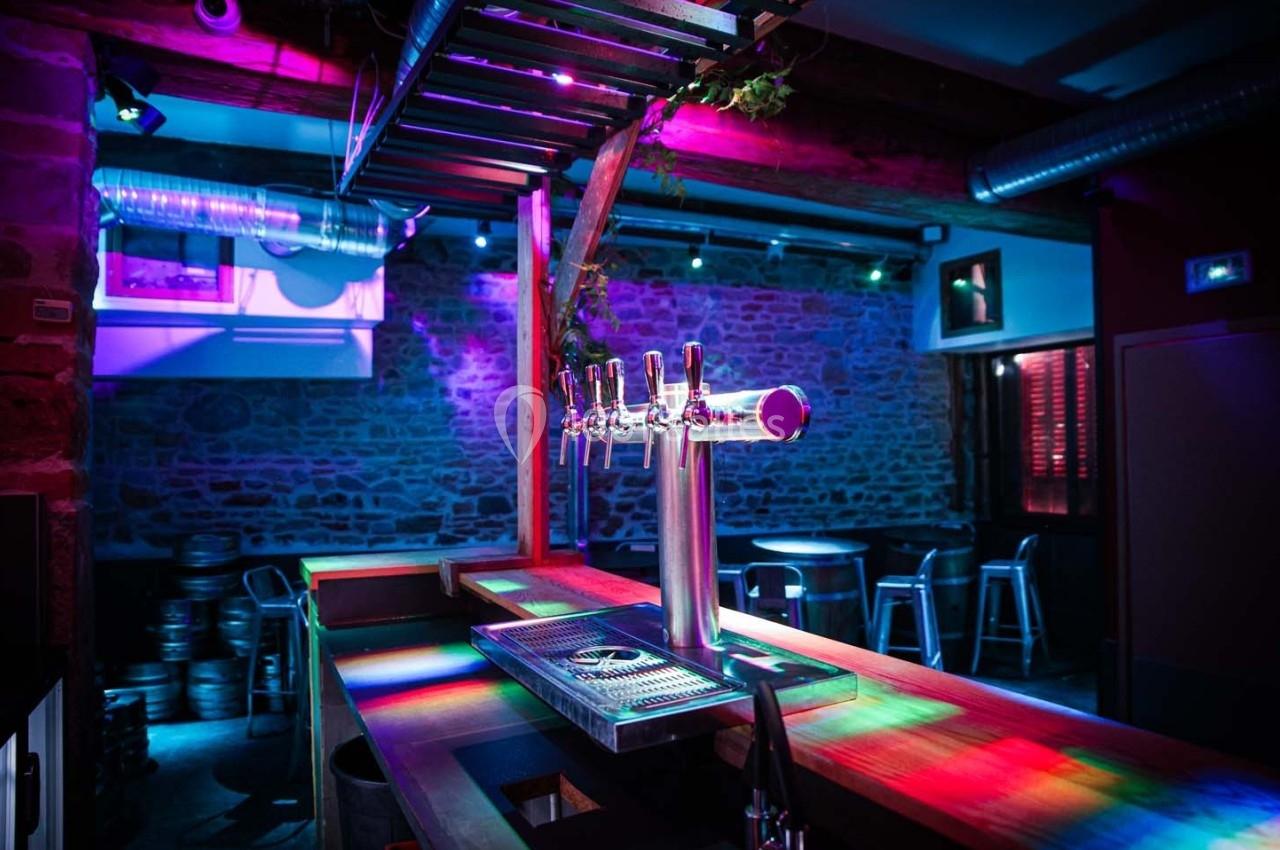 Comptoir de bar avec tireuses à bière, éclairé par des lumières colorées dans une ambiance nocturne.