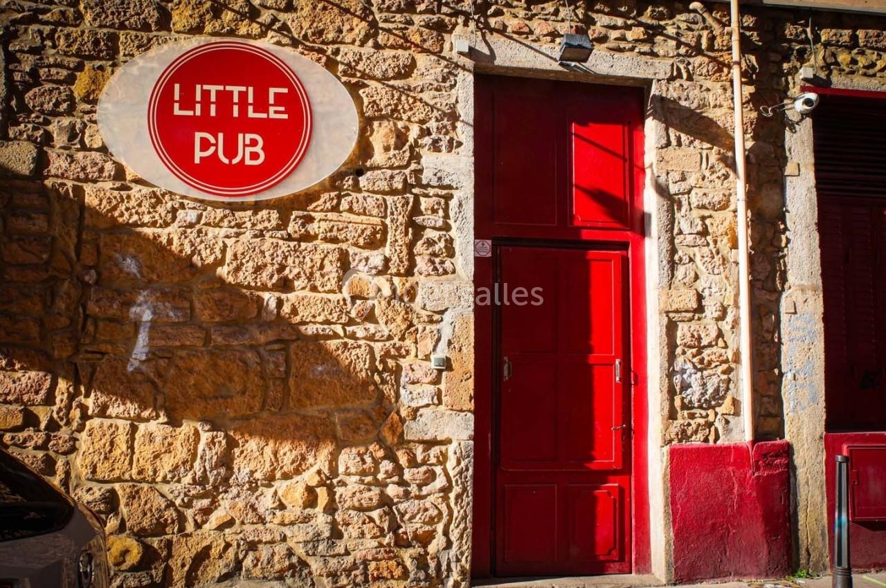 Façade en pierre avec une porte rouge et une enseigne ronde indiquant ’Little Pub’.