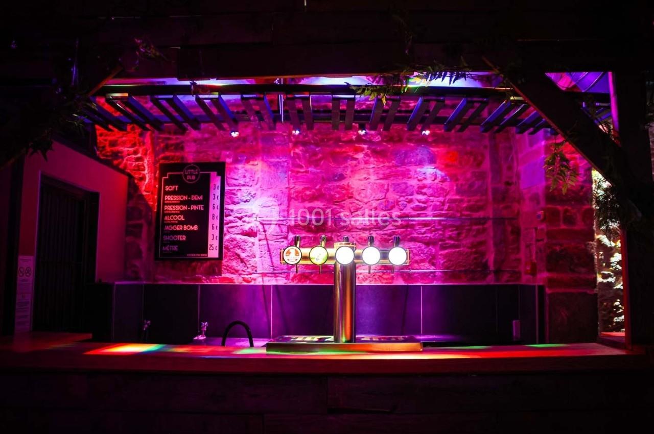 Comptoir de bar avec tireuses à bière illuminé par des lumières colorées dans un décor en pierre.