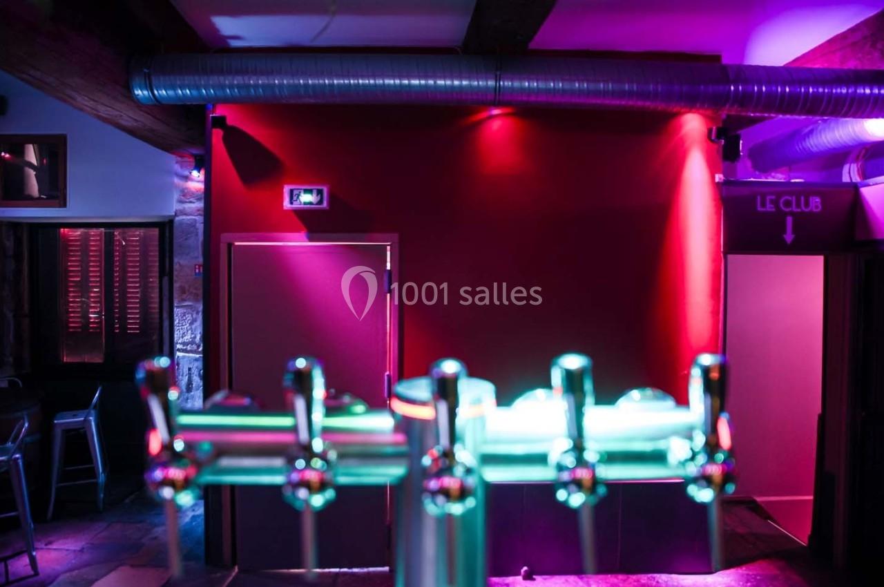 Robinet de bar en métal au premier plan, avec un mur rouge et un éclairage coloré en arrière-plan.