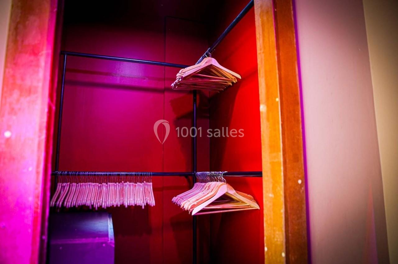 Portant en bois dans une armoire ouverte, éclairée par une lumière rose, avec plusieurs cintres suspendus.