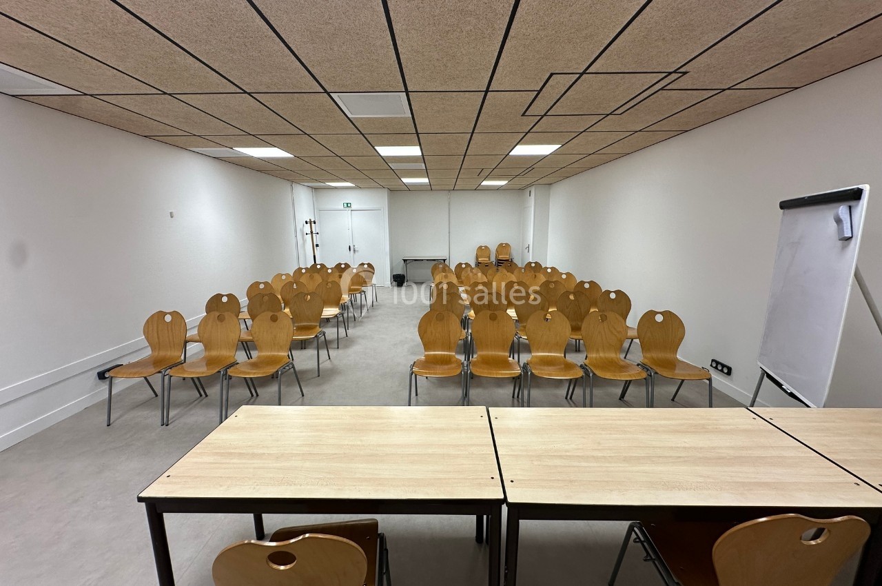 Salle de réunion avec des rangées de chaises en bois, un tableau blanc et des tables au premier plan.