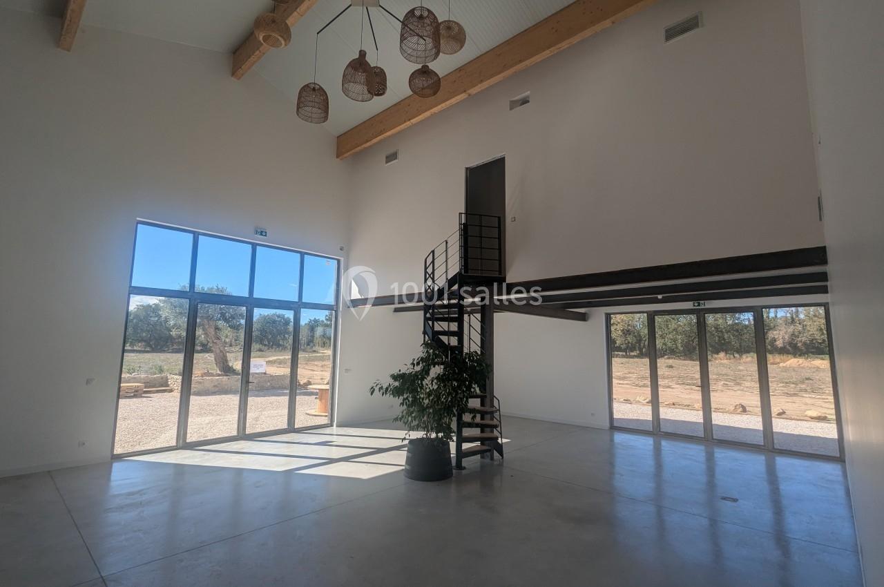 Intérieur lumineux avec mezzanine, escalier métallique, grandes baies vitrées et vue sur un paysage extérieur.