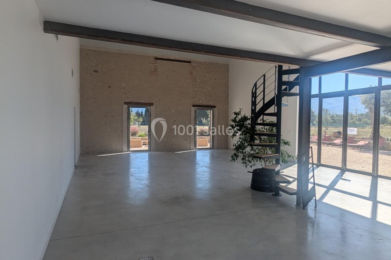 Intérieur d'une pièce lumineuse avec sol en béton, murs clairs, escalier métallique et grandes baies vitrées donnant sur l…