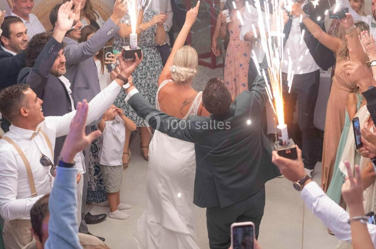 Un couple de mariés danse entouré d'invités tenant des fontaines lumineuses dans une salle festive.