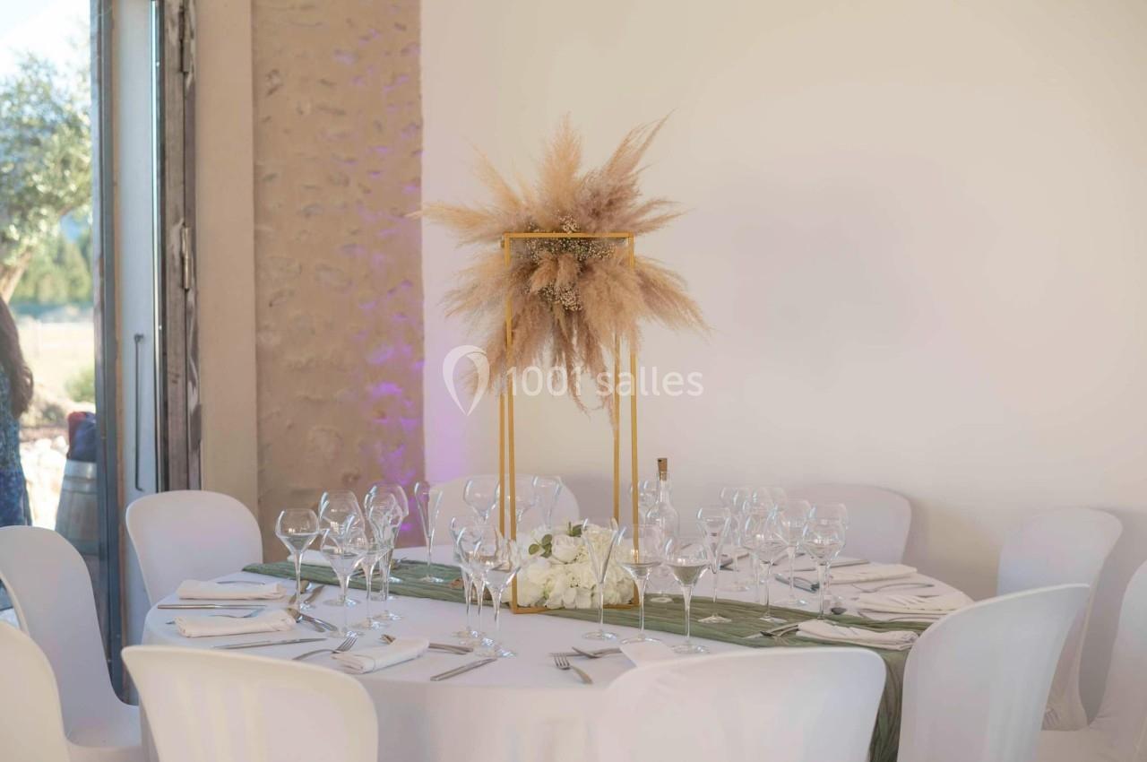 Table ronde décorée pour un événement, avec nappes blanches, centre de table en pampas et vaisselle élégante.
