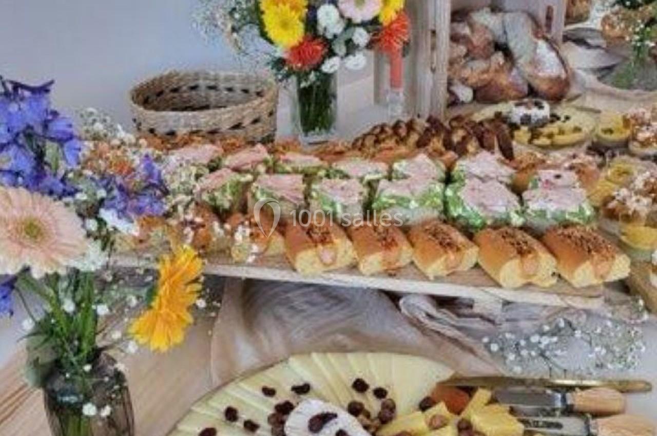 Buffet composé de pains garnis, plateaux de fromages et fleurs décoratives sur une table en bois.