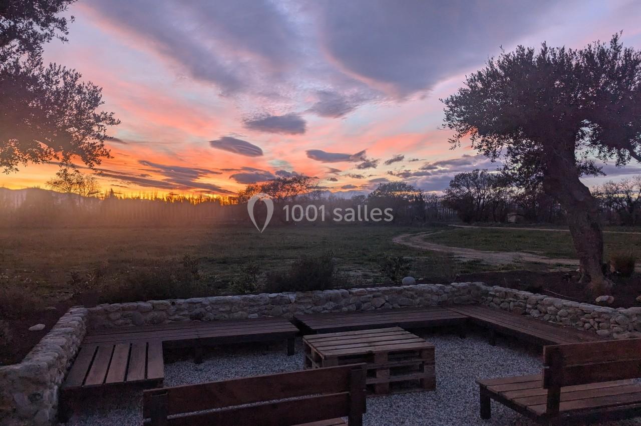 Coucher de soleil coloré sur un paysage rural avec des bancs en bois entourés d'oliviers et d'un chemin de terre.