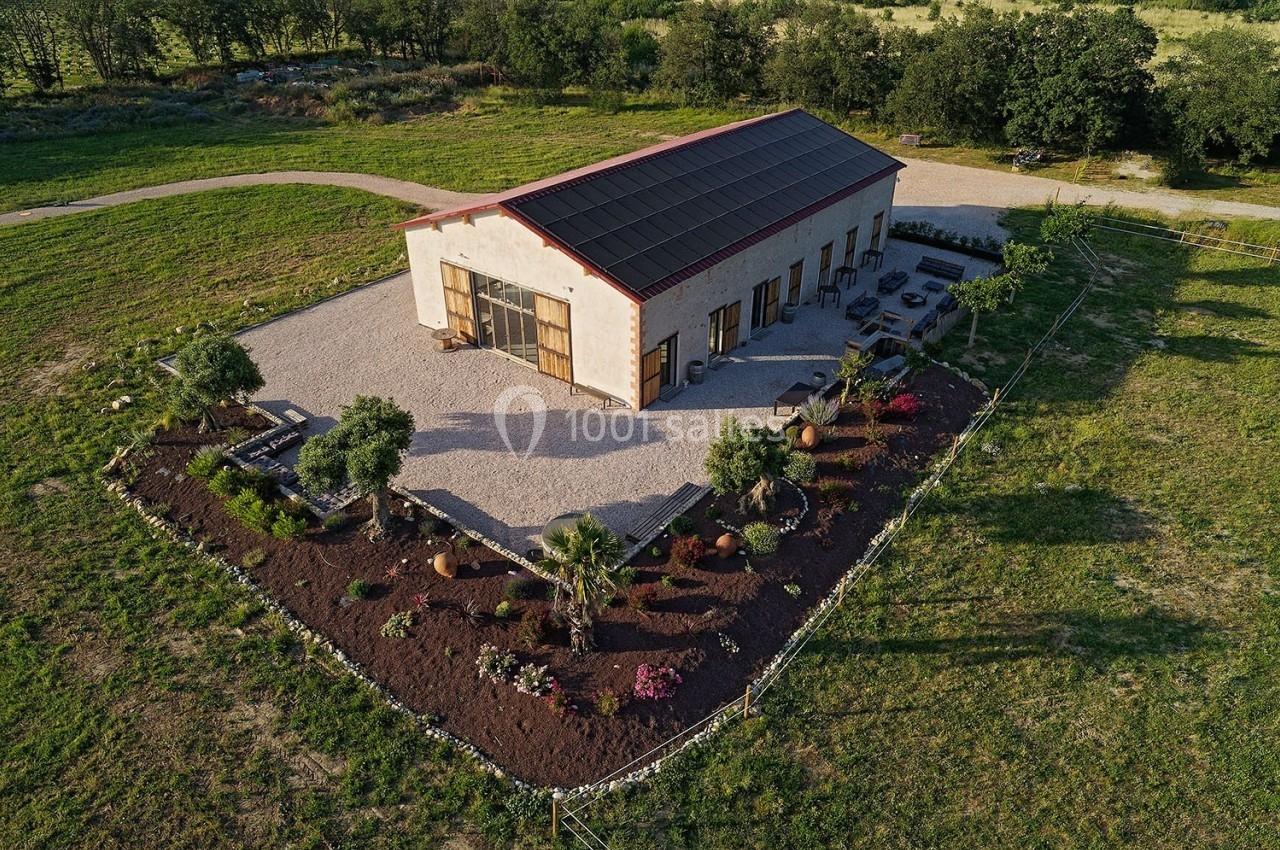 Bâtiment moderne avec toit solaire entouré d'un jardin paysager et d'une allée en gravier, vu en perspective aérienne.
