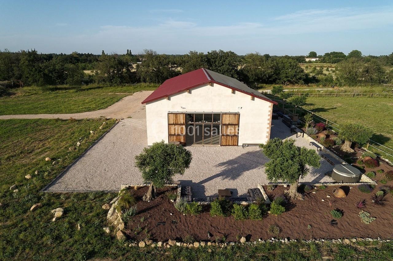 Bâtiment avec toit rouge entouré de végétation, allée en gravier et jardin aménagé, situé en pleine campagne.