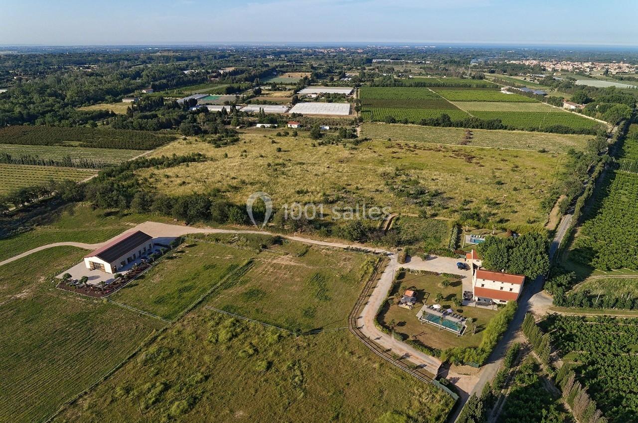 Vue aérienne d'une zone rurale avec champs, bâtiments agricoles et une maison avec piscine entourée de verdure.