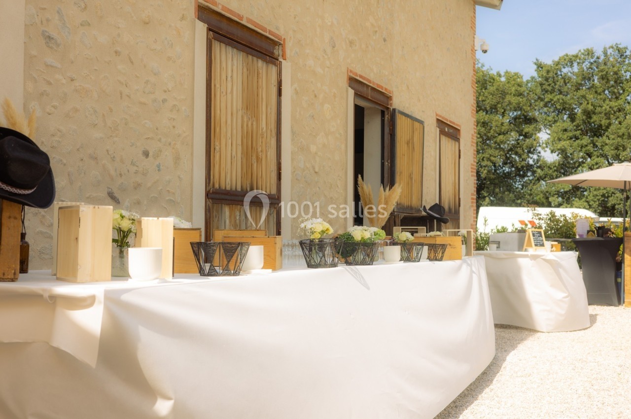 Tables décorées avec des fleurs et des objets en bois devant un bâtiment en pierre, sous un ciel ensoleillé.